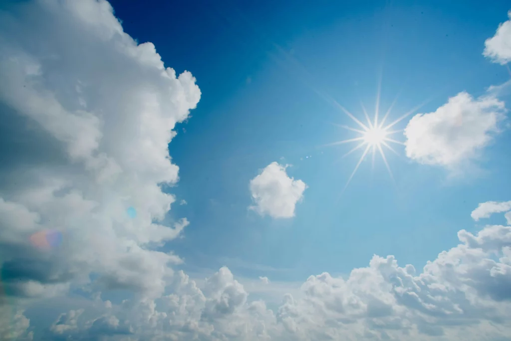 Soleil éclatant rayonnant dans un ciel bleu azur parsemé de nuages.