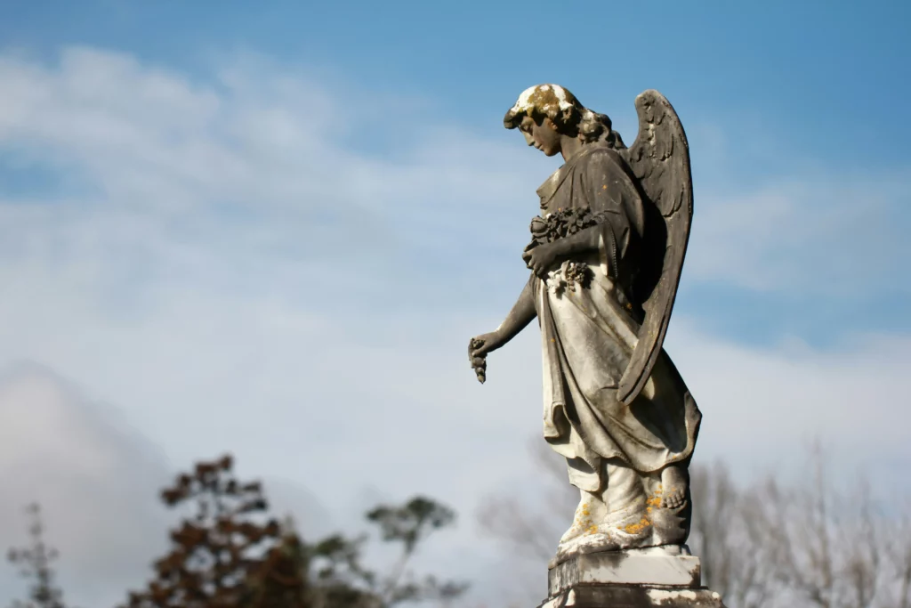 Statue d'ange sculptée en pierre sur fond de ciel nuageux.