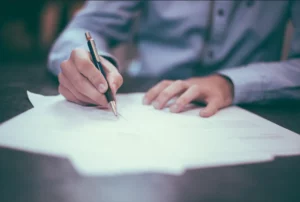 Personne rédigeant un document officiel lors d'un rendez-vous de démarches.